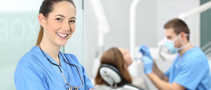 dentist smiling while dental procedures takes place in the background